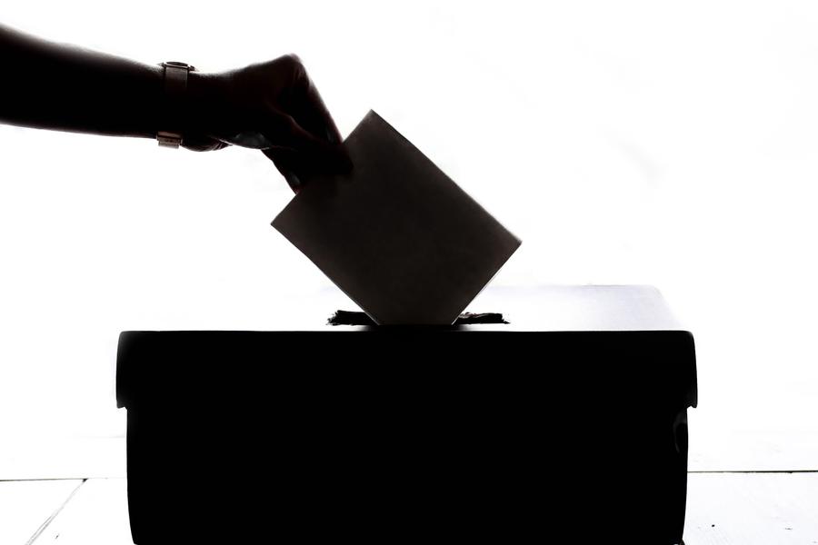 Vote : main tenant un bulletin légèrement enfoncé dans la fente d'une urne en contre-jour